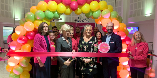 a group of people are cutting a ribbon under a balloon archway